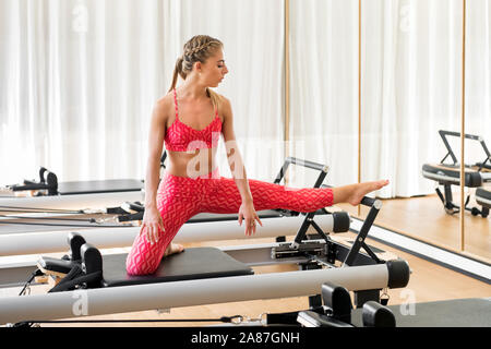 Frau tun leg stretching Übungen in der Turnhalle während der Arbeit aus auf einem Pilates Reformer Bett in einem Gesundheit und Fitness Concept Stockfoto