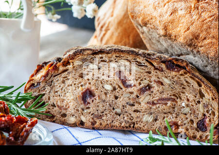 Frisch gebackenem Roggenbrot mit Samen und Rosinen auf sauerteig ohne Hefe mit getrockneten Tomaten Rosmarin und Thymian. Hausgemachte Kuchen. Stockfoto