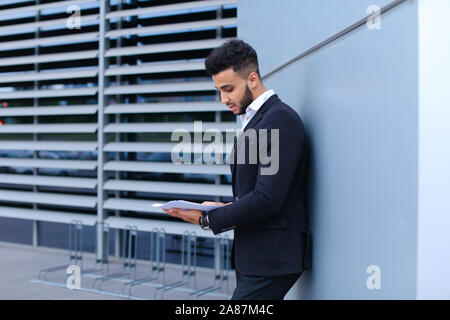 Junge Unternehmer Asiaten hält und hält, liest und sortiert Papiere, steht in der Nähe der Wand des Business Center. Stockfoto