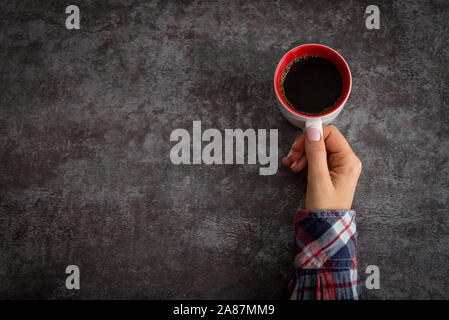 Weibliche Hände halten Kaffeetasse über dunkle Tabelle Stockfoto