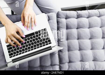 Weibliche Hände schreiben auf Laptop Tastatur grau Kissen Hintergrund. Stockfoto