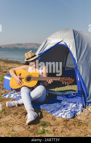 Frau Tourist mit Gitarre sitzt neben Zelt. Stockfoto