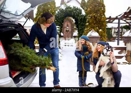 Vater brachte Weihnachtsbaum in der große Kofferraum der SUV-Auto. Tochter, Mutter und Hund treffen Vati ihn gerne mit Holidays Home Dekorationen. Familie Stockfoto
