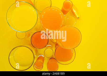 Abstrakte Komposition Blick von oben auf die orange und gelb Säfte Getränke in verschiedener Form Gläser mit Orangenscheiben Obst und auf gelbem Hintergrund Stockfoto