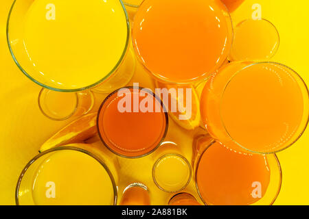 Abstrakte Komposition Blick von oben auf die orange und gelb Säfte Getränke in verschiedener Form Gläser mit Orangenscheiben Obst und auf gelbem Hintergrund Stockfoto