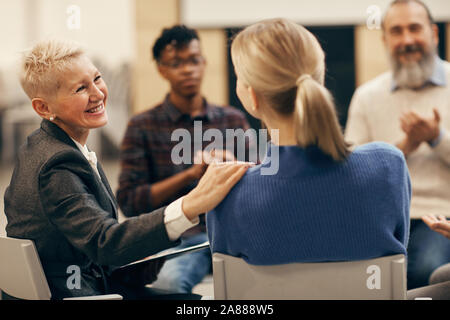 Lächelnd reife Frau mit kurzen Haaren im Gespräch mit der jungen Frau während der Therapie Lektion Stockfoto