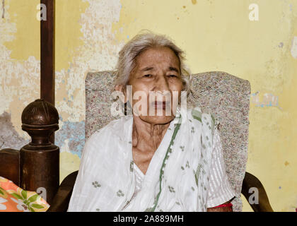 Portrait von lächelnden Active Senior asiatischen und indischen Ethnizität Frau von 82 Jahren auf Stuhl ruht, zu Hause zu sitzen, während bei Kamera schaut. Stockfoto