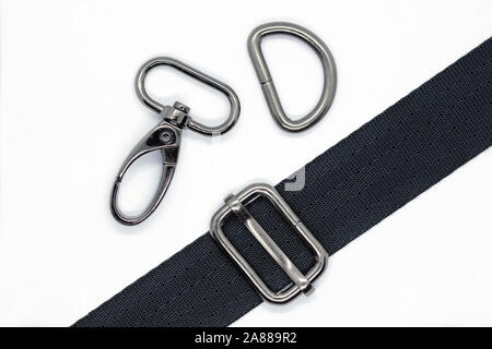 Nähen von Beschlägen für die Herstellung von Taschen und Rucksäcken. Karabiner, halben Ring und Höhenversteller in dunklen Nickel Farbe auf weißem Hintergrund. Schwarzes Band für Stockfoto