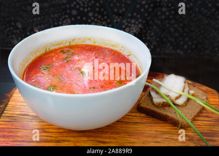 Eine Platte mit einem roten borscht auf dem Tisch. Mittagsmenü Borscht mit Sauerrahm und Roggenbrot mit Speck und Zwiebeln. Köstliche pflegende h Stockfoto