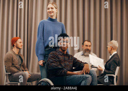 Porträt der jungen Frau mit Afrikanischen behinderte Mann an der Kamera lächelnd zusammen beim Besuch Therapie Klasse Stockfoto