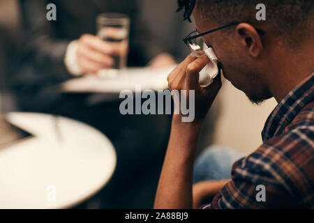 Ansicht der Rückseite des Afrikanischen jungen Mann, seine Tränen abwischen mit Serviette während der Anhörung auf Psychologe Stockfoto