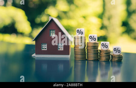 Symbol für sinkende Zinsen. Mit prozentualer Symbole auf abnehmende hohen Stapel von Münzen neben einem Modell Haus Würfel. Stockfoto