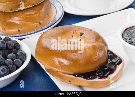 Eine geschnittene blueberry Bagel mit Heidelbeere Konfitüre gefüllt. Es gibt Beilagen von biologischem Obst und bewahrt. Stockfoto