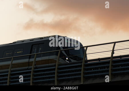 Zug miteinem mdoern Design bewegen durch eine Brücke. Wolken und warmen roten Himmel im Hintergrund. Stockfoto