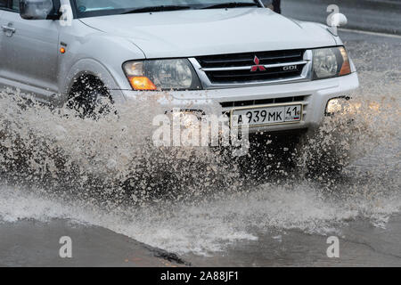 Nahaufnahme der japanische SUV Mitsubishi Pajero fahren auf überschwemmte Straße Straße über Tiefen schlammigen Pfütze, Spritzer Tropfen Spritzwasser von den Rädern durin Stockfoto