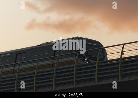 S-Bahn mit modernen Design, die durch eine Brücke mit roten Skyline und den Sonnenuntergang Wolken im Hintergrund. Stockfoto