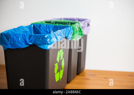 Hand alte Zeitungen in den Papierkorb. Person im Haus Küche Trennung von Abfällen. Schwarz Papierkorb mit der blauen Tasche und recycling Symbol. Stockfoto