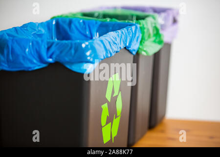 Hand alte Zeitungen in den Papierkorb. Person im Haus Küche Trennung von Abfällen. Schwarz Papierkorb mit der blauen Tasche und recycling Symbol. Stockfoto