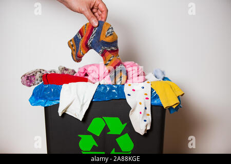 Hand verwendet Socke in bin mit Recycling zu unterzeichnen. Person im Haus Trennung von Abfällen. Haufen bunte Kleidung in der Black Box. Textile Auslastung c Stockfoto