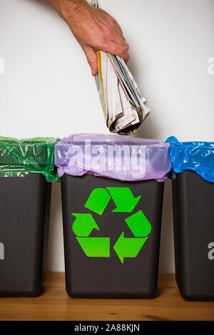 Hand alte Zeitungen in den Papierkorb. Person im Haus Küche Trennung von Abfällen. Schwarz Papierkorb mit der blauen Tasche und recycling Symbol. Stockfoto