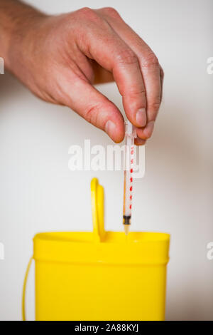 Hand benutzte Spritze mit Nadel in die gelbe Tonne für sichere Entsorgung. Person die Trennung gefährlicher Abfälle. Medizinische Abfälle Stockfoto