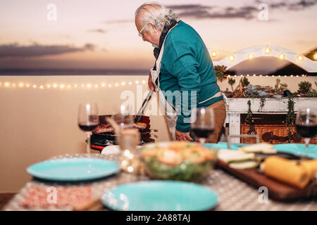 Ältere Menschen Grillen von Fleisch am Grill Abendessen auf der Terrasse - Großvater Kochen für seine Familie auf dem Dach Stockfoto
