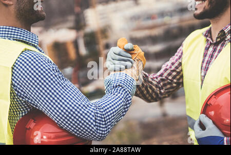 Junge Baumeister die Hände schütteln, dass ein Abkommen über die Baustelle - Arbeitnehmer erreichen ein Abkommen und auf der Arbeit Projekt Stockfoto