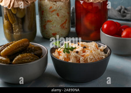 Hausgemachten Sauerkraut, gesalzene Tomaten und Gurken in eine Schüssel und ein Glas Gläser auf einem hellblauen Hintergrund, Konzept fermentiertes Gemüse Stockfoto