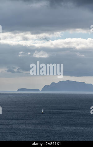 Eine kleine Yacht segeln auf einer fernen Insel, Sonnenstrahlen, die durch dramatische graue Wolken über Stockfoto