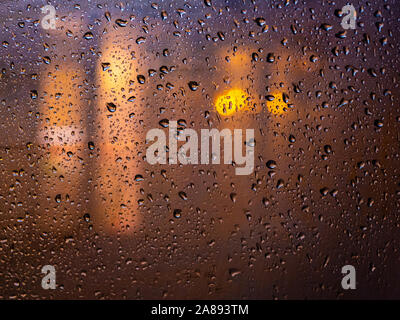 Die Lichter der Nacht Stadt während der Regen hinter ein Glas mit Wasser bedeckt. Abstrakte farbenfrohe verschwommenen Hintergrund. Nasse Muster auf Glas. Stockfoto