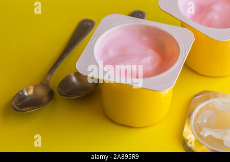 Zwei Erdbeer Joghurt becher mit kleinen silbernen Löffel auf hellen Hintergrund gelb-rosa Joghurtbecher Stockfoto