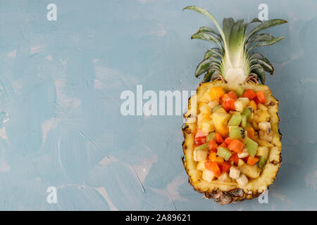 Tropischer Obstsalat in der halben Ananas auf einem hellblauen Hintergrund, horizontale Ausrichtung, Kopieren Raum Stockfoto