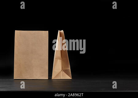 Umweltfreundliches Einweggeschirr. Zwei biologisch abbaubar, braun Handwerk Papiertüten auf eine dunkle Oberfläche vor einem schwarzen Hintergrund. Recycling Konzept. Auch verwenden Stockfoto