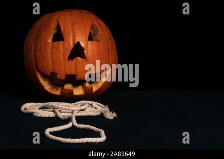 Kürbis ausgesetzt auf einem Seil. Vorbereitung für Halloween. Orange Squash auf einem schwarzen Hintergrund mit einem weißen Seil. Stockfoto