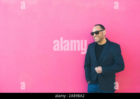 Lächelnder Mann mit Sonnenbrille und Blazer an pinker Wand Stockfoto