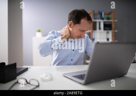 Junge Menschen leiden unter Nackenschmerzen beim Arbeiten am Laptop Stockfoto