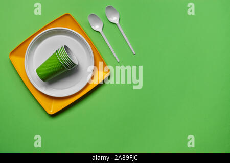 Bunte Kunststoff Einmalgeschirr, wie zwei Teller und Löffel, gefaltet Cups auf grünem Hintergrund mit Kopie Raum. Das Konzept der Picknick Utensil. Stockfoto