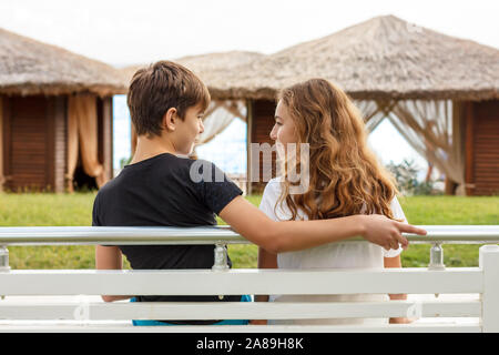 Paar schöne Teens, erste Liebe. Guy Umarmungen ein Mädchen sitzt auf der Bank und einander suchen Stockfoto