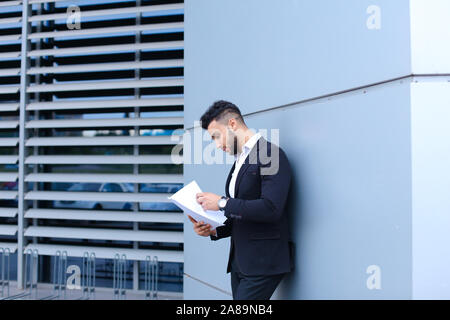 Junge Unternehmer Asiaten hält und hält, liest und sortiert Papiere, steht in der Nähe der Wand des Business Center. Stockfoto