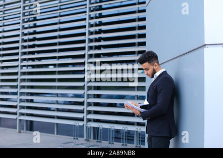 Junge Unternehmer Asiaten hält und hält, liest und sortiert Papiere, steht in der Nähe der Wand des Business Center. Stockfoto