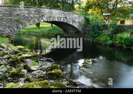 Moos bedeckt Felsen am Ufer des Flusses Rothay in Rydal mit Steinbogen Pelter Bridge Lake District, England Stockfoto