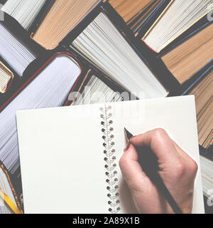 Weibliche Hand schreiben Hinweise auf das Notebook. Vielen bunten Dicken öffnen Bücher stehen auf einem dunklen Hintergrund Stockfoto