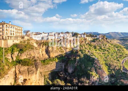 Ronda, Spanien: Landschaft der weißen Häuser am grünen Rand der steilen Klippen mit Bergen im Hintergrund. Stockfoto