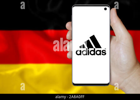 Logo der öffentlichen Unternehmen Adidas auf dem Smartphone angezeigt. Flagge Deutschland Hintergrund. Credit: PIXDUCE Stockfoto