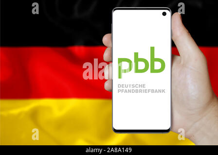 Logo der öffentlichen Unternehmen Deutsche Pfandbriefbank AG auf dem Smartphone angezeigt. Flagge Deutschland Hintergrund. Credit: PIXDUCE Stockfoto