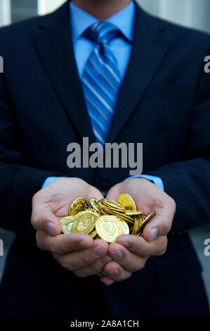 Nicht erkennbare Geschäftsmann Holding eine Handvoll gold Schatz Münzen stehen draußen in einen dunklen Anzug Stockfoto