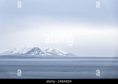 Ferne und undeutlich die schneebedeckten Berge eingehüllt in Nebel Nebel und Wolken auf einem fernen Küstenlinie von offenen Ozean erscheinen Stockfoto