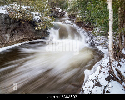 Einen Stream hetzt, um eine Kurve durch eine Zeder und Birkenwälder im Winter Stockfoto