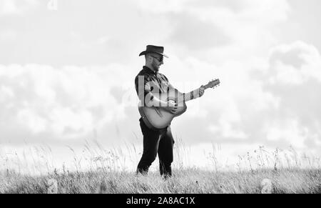 Inspiriert land Musiker. Landhausstil. Sommer Urlaub. Country Music Konzept. Gitarrist Land Sänger stand im Feld Himmel Hintergrund. Wandern Song. United mit der Natur. Stattlicher Mann mit Gitarre. Stockfoto