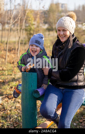 Mutter - ein im mittleren Alter Junge brünette Frau spielt mit ihrem dreijährigen Sohn an einem sonnigen Herbsttag. Fröhliche Stimmung, lächeln Stockfoto